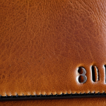 ** A close-up shot showcasing the texture and natural markings of full-grain leather. The image should highlight the leather's imperfections (scars, wrinkles) and its rich color. The leather item is a wallet that shows usage with slight wear marks.

**